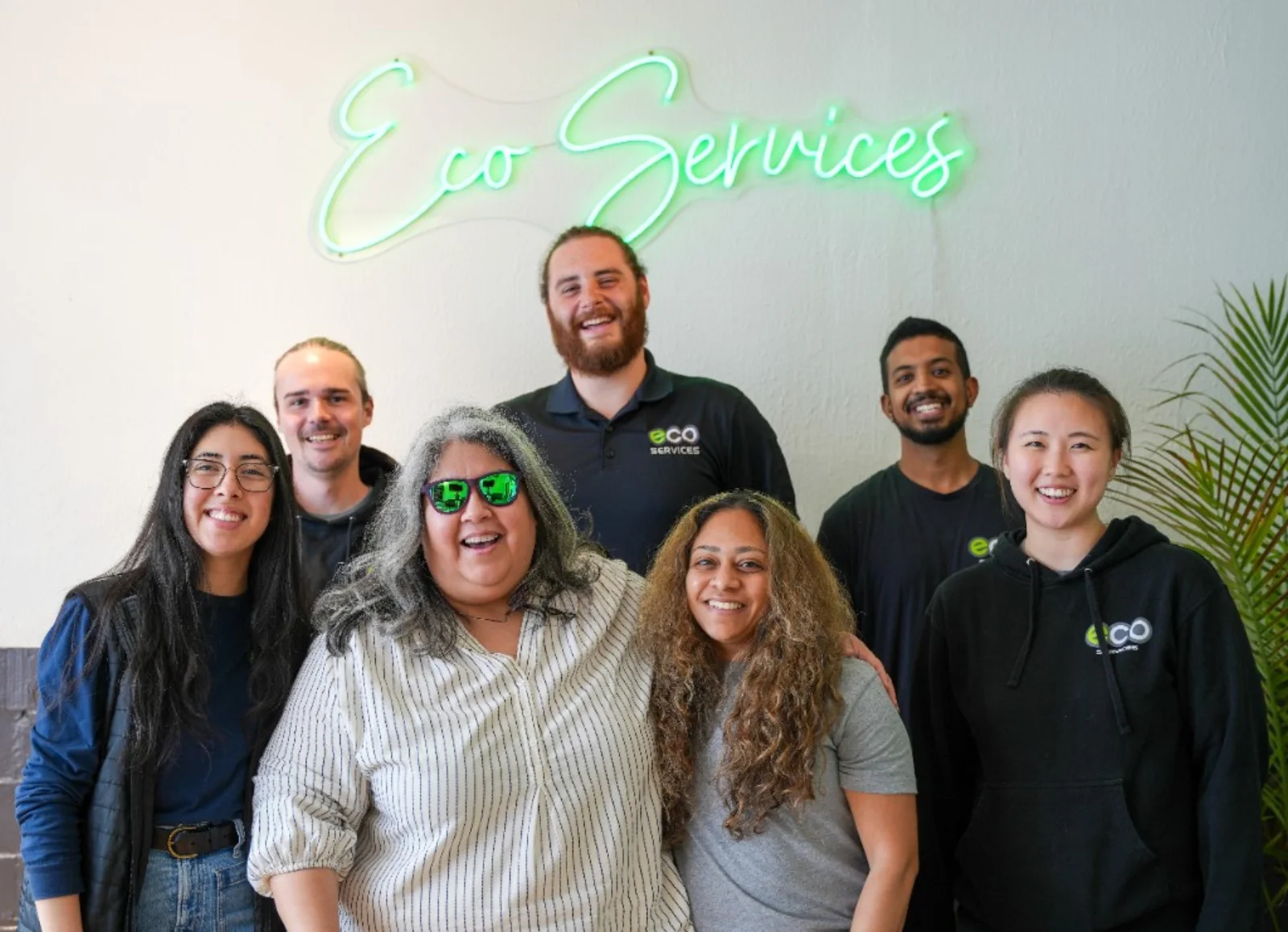 Seven Eco team members under the Eco Services neon sign at the office