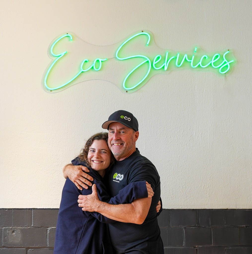 Eco Electric, Plumbing, Heating & Air leadership sharing a hug under the Eco Services sign