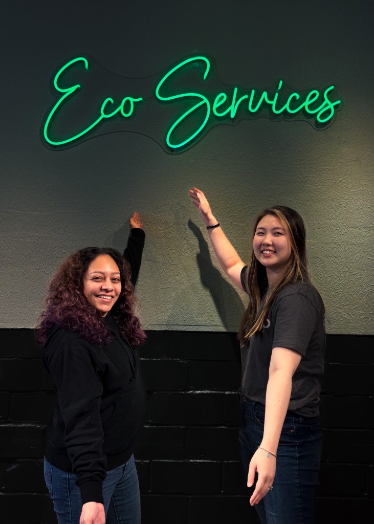 Two Eco team members under the Eco Services neon sign
